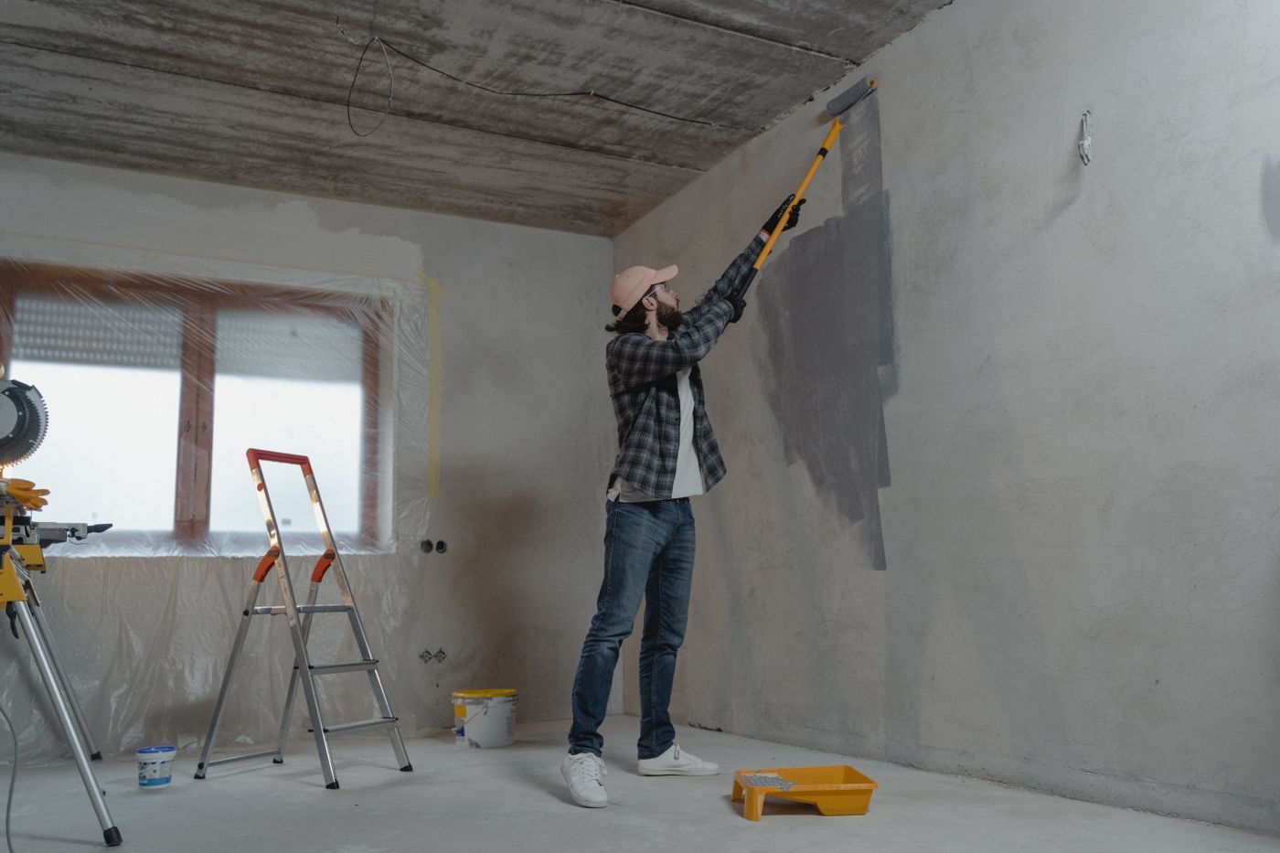 Schilder verft met een roller op lange steel een grijze muur in een kale ruimte